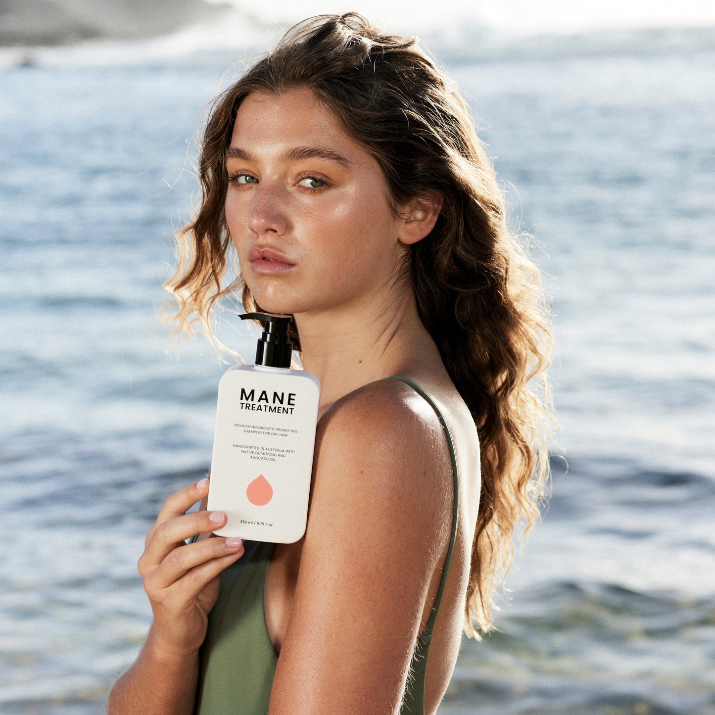 Model holding Mane Treatment nourishing, growth promoting Australian Native shampoo at beach by Hub for Belle