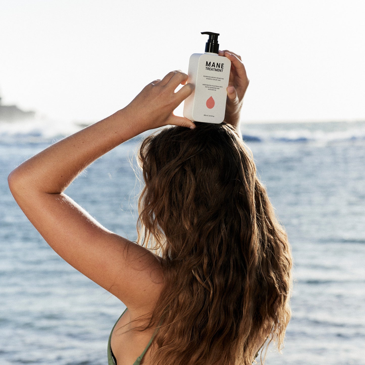 Model holding Mane Treatment nourishing, growth promoting Australian Native shampoo at beach by Hub for Belle