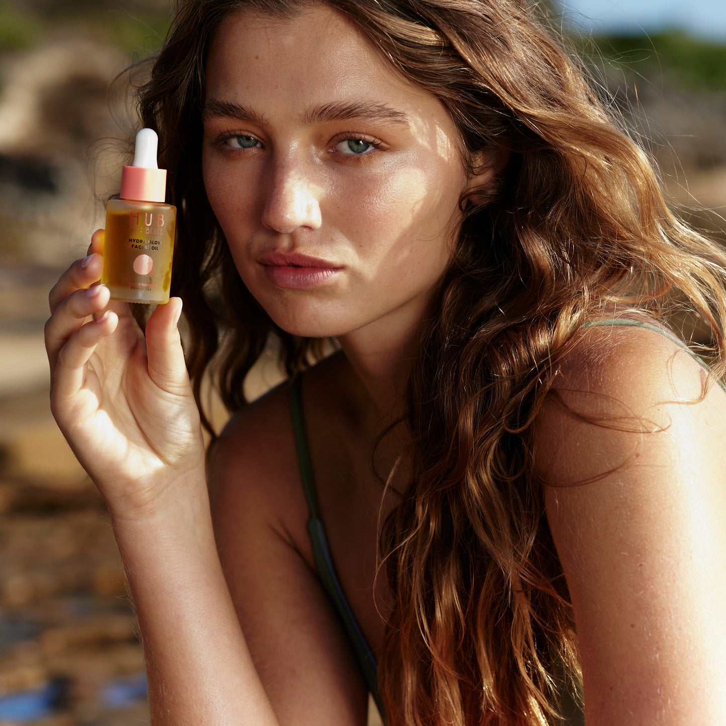 Model holding to face a bottle of Hydra Glow Facial oil balancing made with vegan Australian botanicals for glowing skin from Hub for Belle