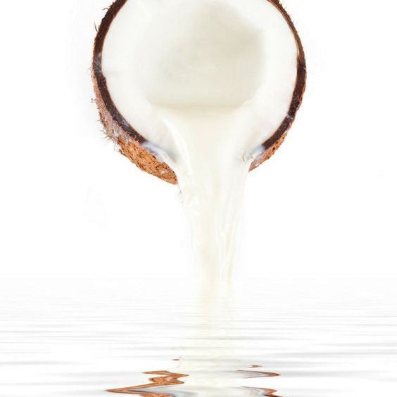 Coconut being sliced open with coconut milk spilling out onto a white surface.