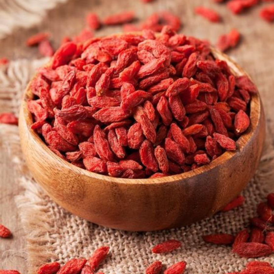 Wooden bowl filled with red goji berries on a textured surface