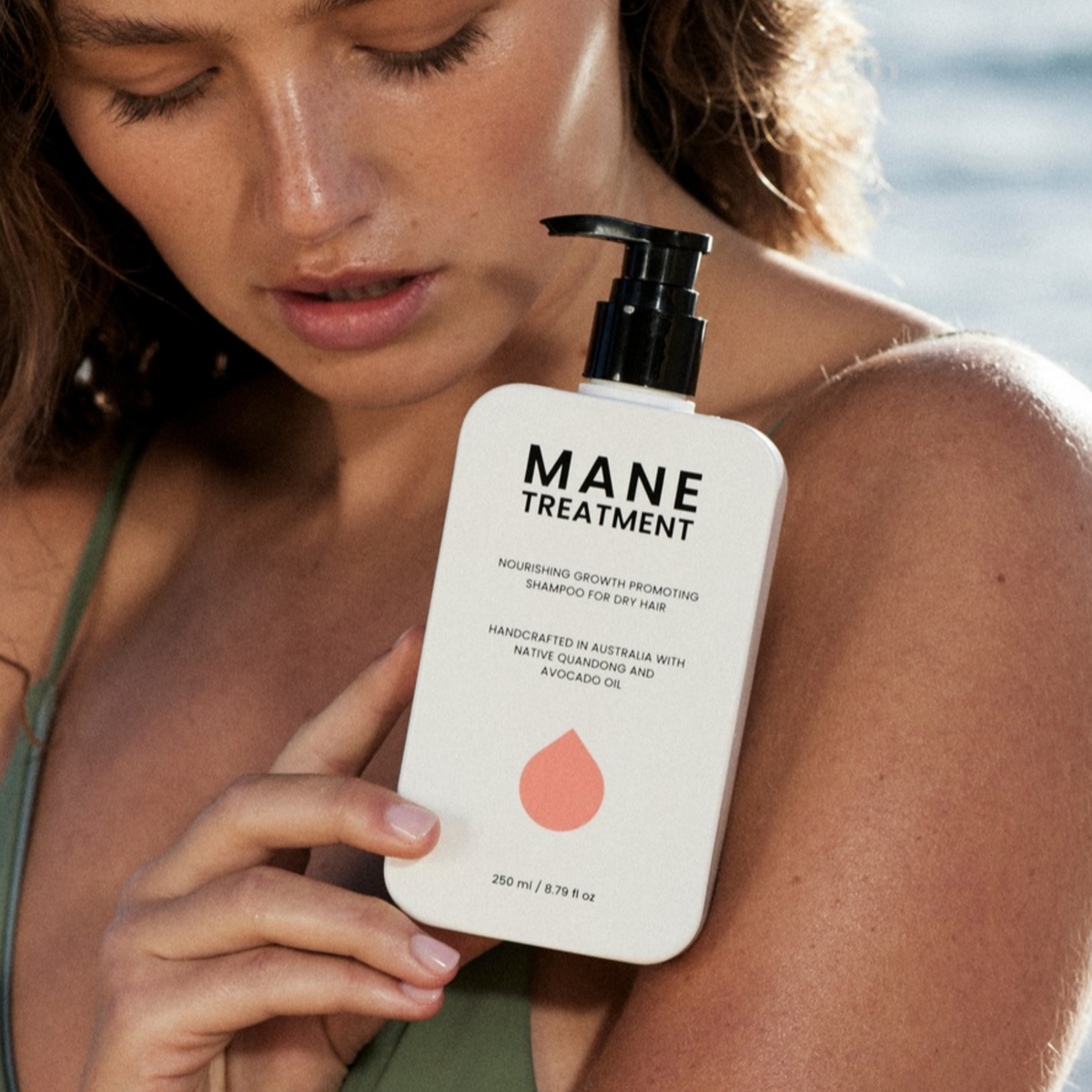 Model holding Mane Treatment by Hub for Belle nourishing, growth promoting Australian Native shampoo at beach.