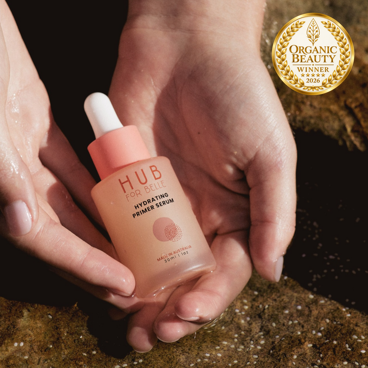 Hub For Belle Hydrating Primer Serum being held by hands in a rock pool at the beach, alongside an Organic Beauty Winner 2026 badge.